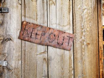 Rusty sign reading 'KEEP OUT'. It is hanging on an old weathered wooden door. Horizontal shot.