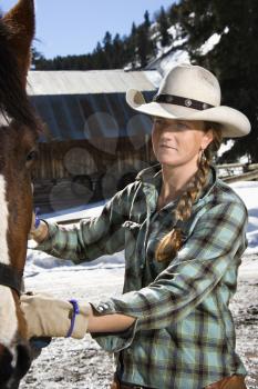 Attractive young woman wearing a cowboy hat and petting a horse. Vertical shot.
