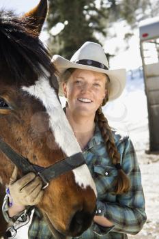Attractive young woman in a cowboy hat, holding a horse and smiling. Vertical shot.