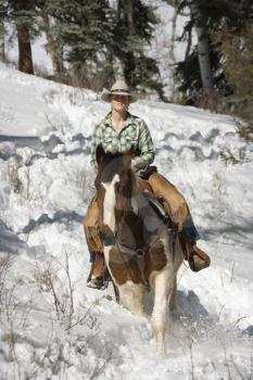 Attractive young woman riding a horse in the snow. Vertical shot.