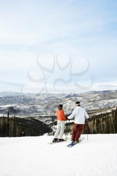 Rear view of skiers on ski slope with mountains in background. Vertical shot.