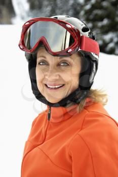 Closeup of smiling female skier wearing red goggles and orange ski jacket. Vertical shot.