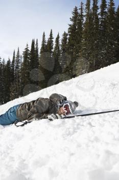 Fallen skier lying on a ski slope in the snow and smiling at camera.  Vertical shot.