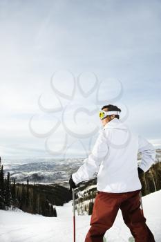 Rear view of a male adult skier on a Colorado ski slope with mountains in background. Vertical shot.