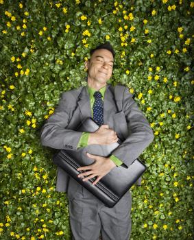 Young businessman with briefcase relaxing in a flower patch smiling with contentment.