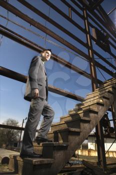 Young businessman walks up a wooden staircase in an abandoned building. Vertical shot.