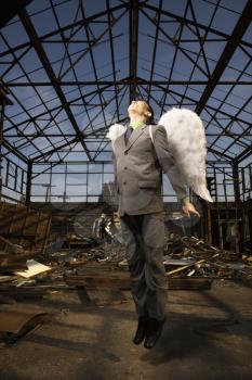 Young businessman with angel wings attempts flight in an abandoned building. Vertical shot.