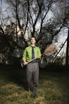 Young businessman standing near the woods with a shovel in hand. Vertical shot.