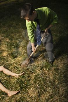 Young businessman uses a shovel to bury a womans body out in a field. Vertical shot.