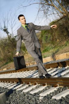 Young businessman with briefcase walks and balances on railroad tracks. Vertical shot.