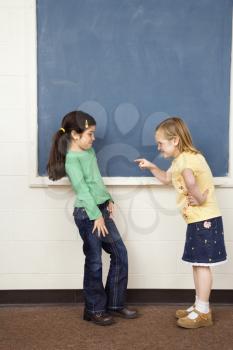 Girl pointing finger at other girl in school classroom. Vertically framed shot.