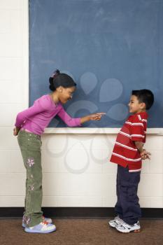 Girl pointing finger at boy in school classroom. Vertically framed shot.
