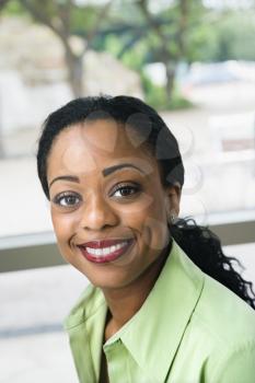 Attractive black woman with pulled back hair sits in front of a window and smiles at the camera. Vertical shot.