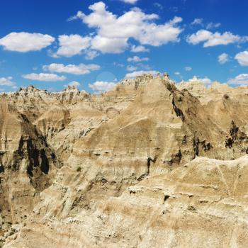 Mountain terrain in Badlands National Park, South Dakota, beneath blue sky and clouds. Square format.