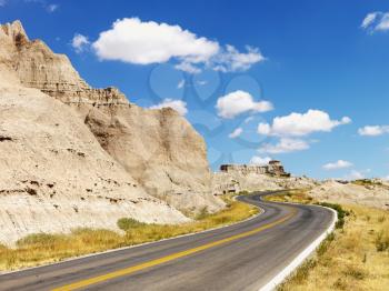 Rural road by rock formations and a field in Badlands National Park, South Dakota. Horizontal shot.