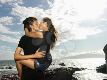 Attractive young couple in a passionate embrace and kissing on a rocky coast. Horizontal shot.
