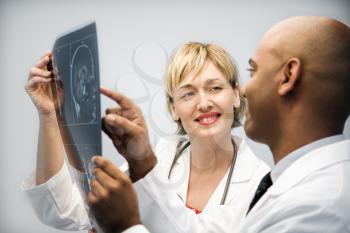 Male and female physicians holding and looking at patient xray film pointing and smiling.