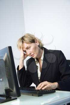 Caucasian businesswoman looking at computer monitor with hand on head looking tired and stressed.