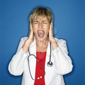 Caucasian female doctor holding hands to ears and screaming.