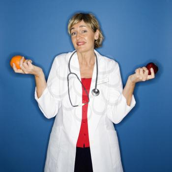 Caucasian female doctor holding apple in one hand and orange in the other.