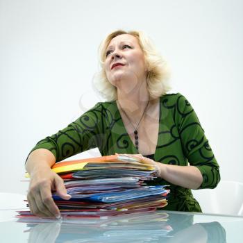 Caucasian middle aged businesswoman sitting at office desk with pile of folders.