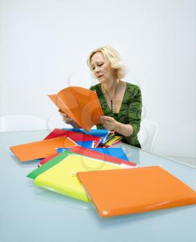 Caucasian middle aged businesswoman sitting at office desk going through pile of folders.