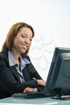 Portrait of African American businesswoman sitting at office desk smiling and looking at computer monitor.