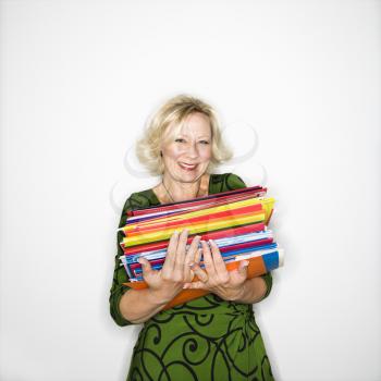 Caucasian middle aged businesswoman carrying stack of folders smiling.
