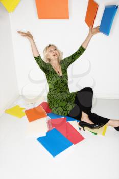 Caucasian middle aged businesswoman sitting on floor throwing stack of work folders into air.