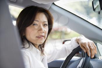 Asian woman sitting in car at steering wheel.