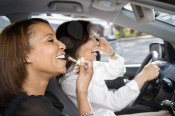 Women distracted and laughing in car with cellphone and cosmetics.