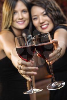 Two attractive young women toasting wine glasses with red wine and smiling.