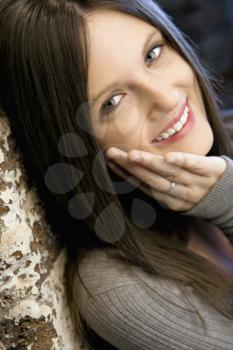 Portrait of pretty young Caucasian woman leaning against brick wall smiling.