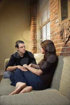 Young Caucasian couple sitting on living room sofa holding hands.