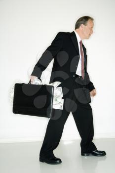 Caucasian middle aged businessman carrying briefcase overflowing with money.