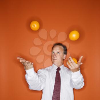 Caucasian middle aged businessman juggling oranges.