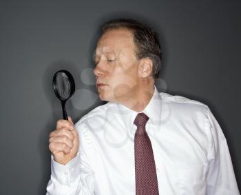 Caucasian middle aged businessman looking through magnifying glass.