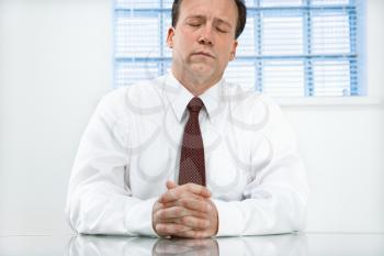 Caucasian middle aged businessman sitting at desk with eyes closed.