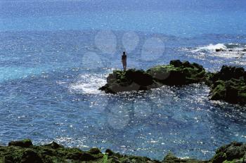Royalty Free Photo of a Woman Standing on Rocks at the Edge of the Water