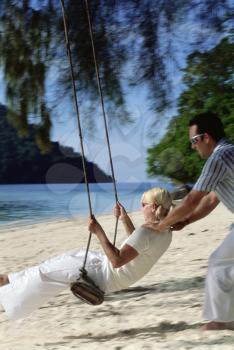 Royalty Free Photo of a Man Pushing a Woman on a Swing at the Beach