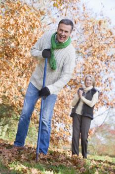 Royalty Free Photo of a Man Raking Leaves With a Woman in the Background