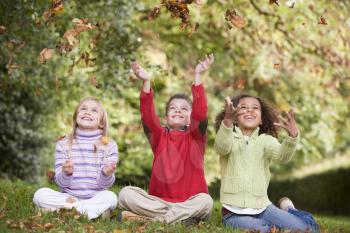 Royalty Free Photo of Three Children Throwing Leaves