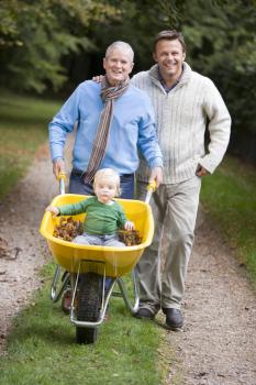 Royalty Free Photo of a Grandfather and Father Pushing a Baby in a Wheelbarrow