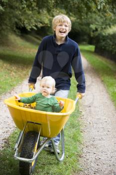 Royalty Free Photo of a Boy Pushing a Baby in a Wheelbarrow