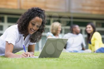 Royalty Free Photo of a Student Working on a Laptop Outside With Others Behind Her