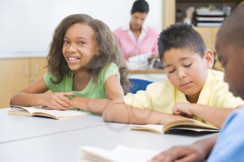 Royalty Free Photo of Students Reading in a Classroom With the Teacher in the Background
