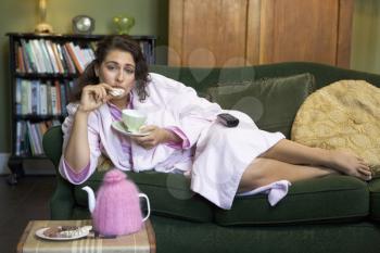 Royalty Free Photo of a Woman Lying on a Sofa Eating Cookies and Drinking Tea