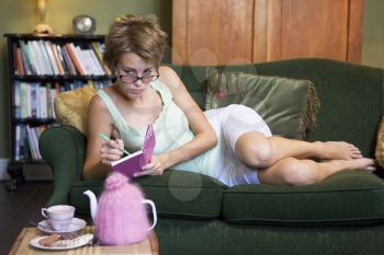 Royalty Free Photo of a Young Woman on a Sofa Writing in a Diary