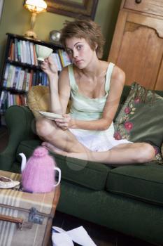 Royalty Free Photo of a Young Woman Sitting on a Sofa Drinking Tea