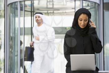 Royalty Free Photo of a Woman With a Laptop and Cellphone And a Man Walking Past